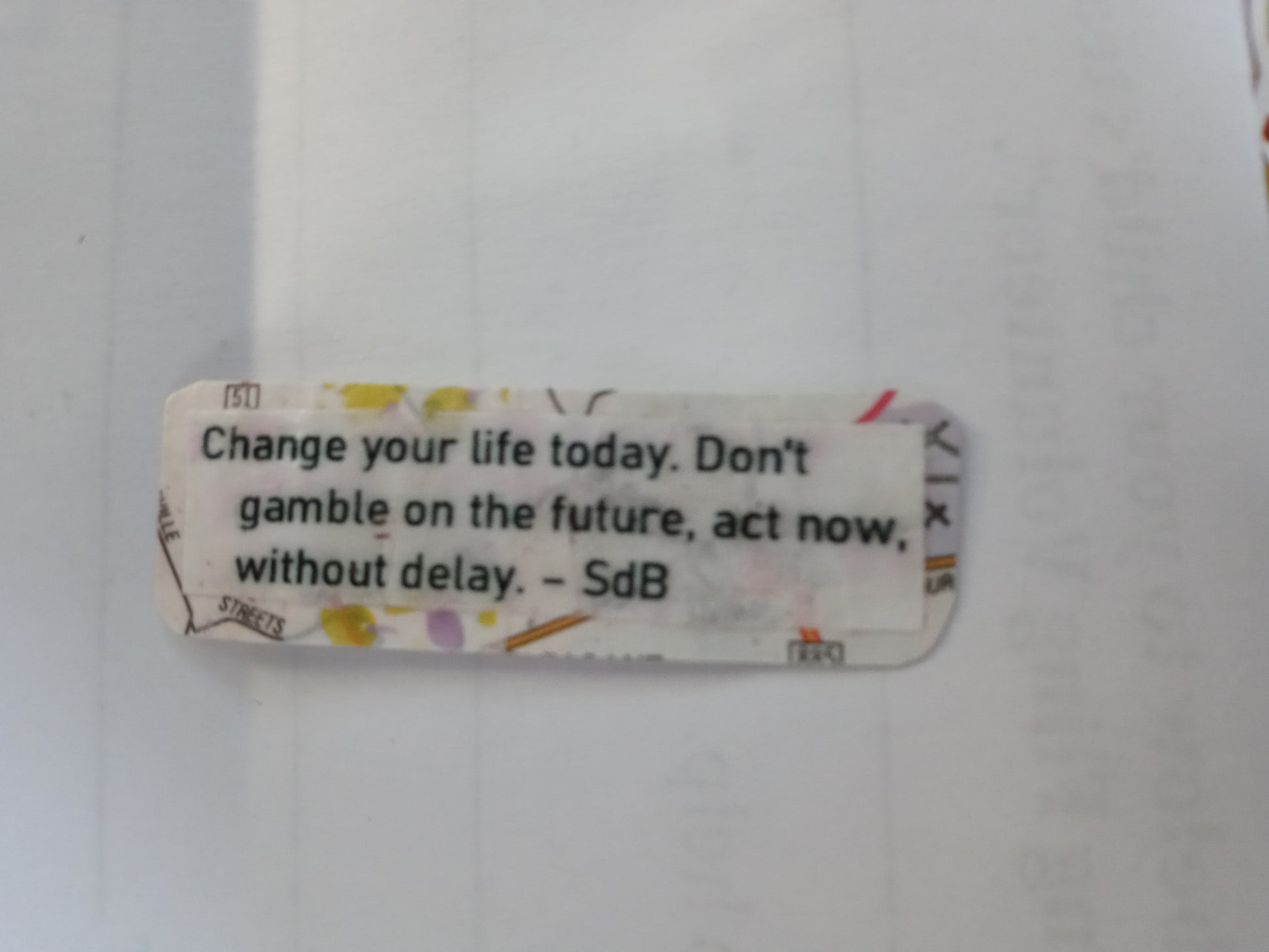 A small handmade sticker of rounded rectangular shape with a map style background. There is a quote overlaid on white paper that reads "Change your life today. Don't gamble on the future, act now, without delay. - SdB"