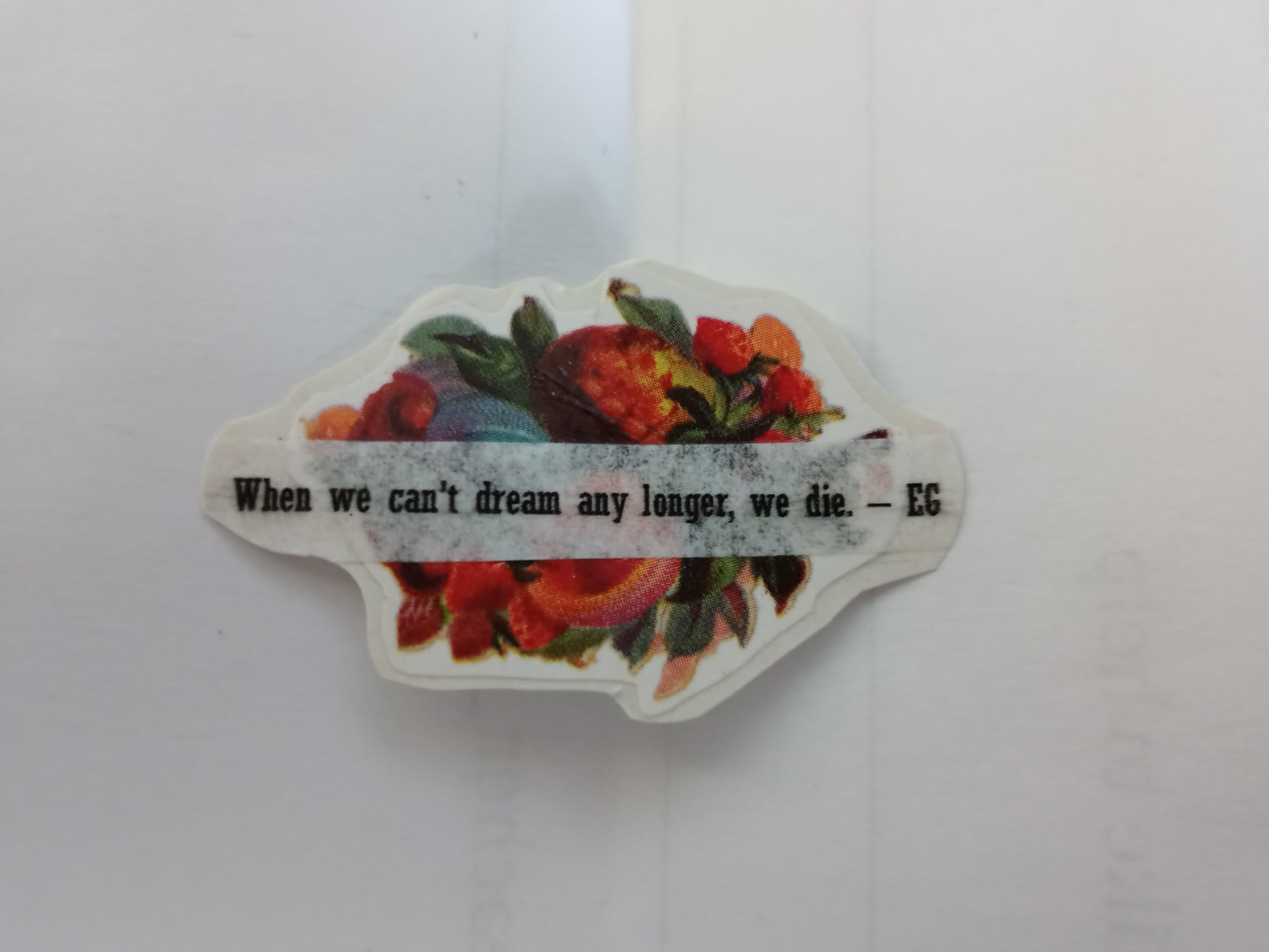 A very small handmade sticker of a Victorian era flower spray with a quote on white paper over top of it that reads "When we can't dream any longer, we die. - EG"